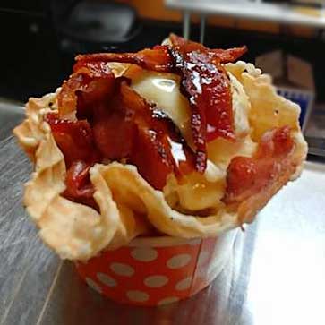 ice cream in a waffle cup topped with pieces of bacon